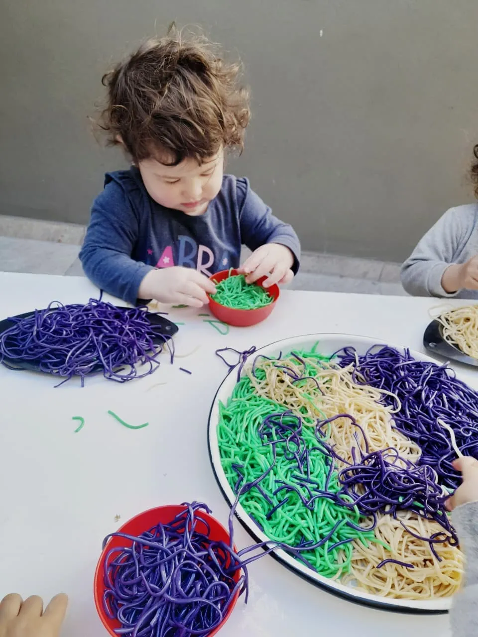 Chicos explorando fideos de colores en una actividad sensorial de la sala