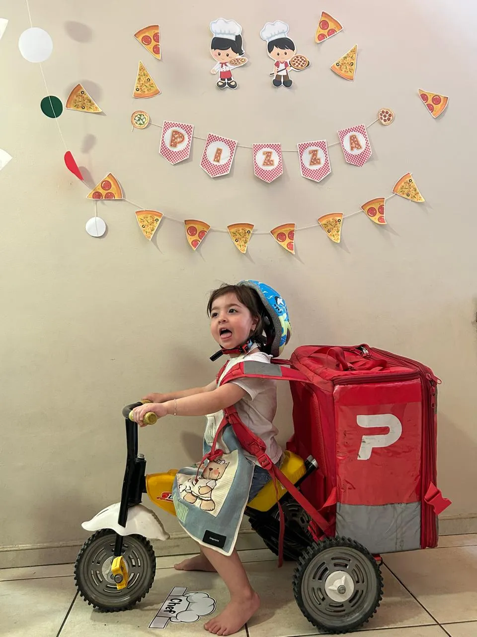 Un nene jugando al delivery de pizza en un triciclo, en la sala